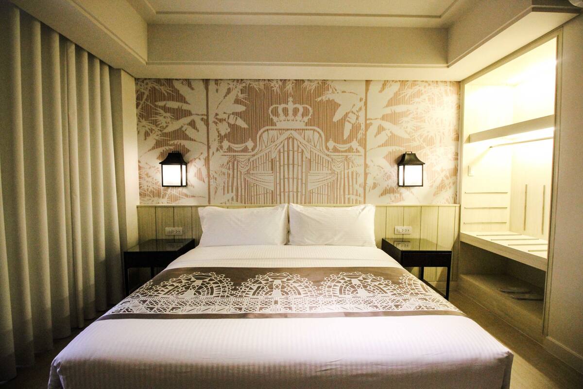 Habitación de hotel con una cama grande, dos mesitas de noche y una lámpara de pared.
