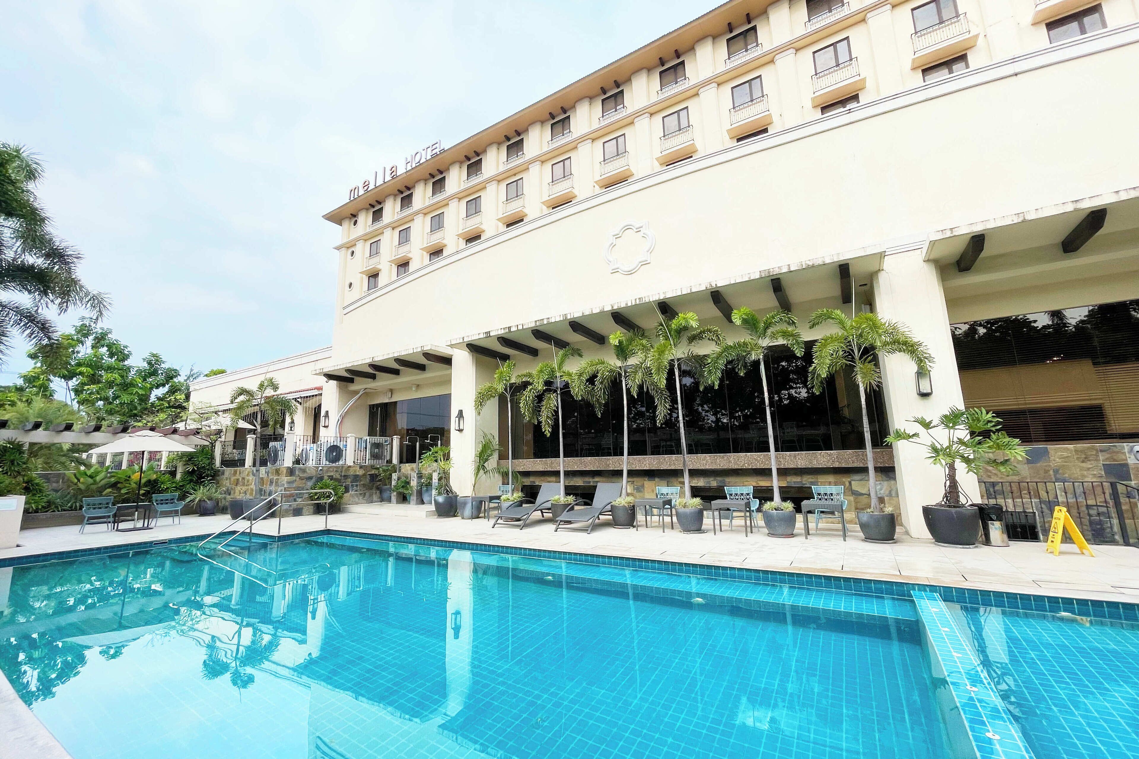 A hotel with a swimming pool, lounge chairs, and potted plants.