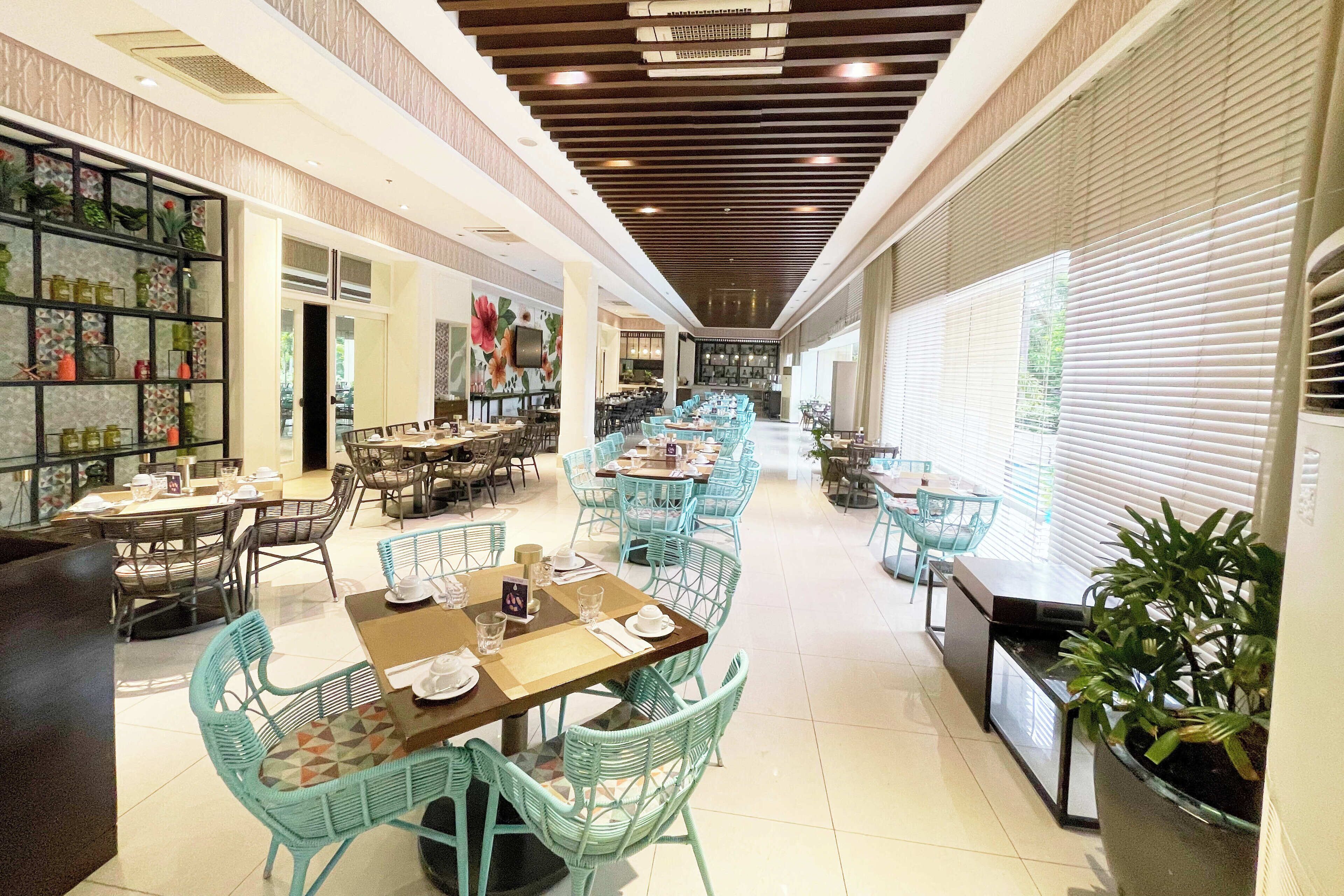 A spacious restaurant with multiple dining areas, including a central open space with tables and chairs, and a side wall with shelves displaying bottles.
