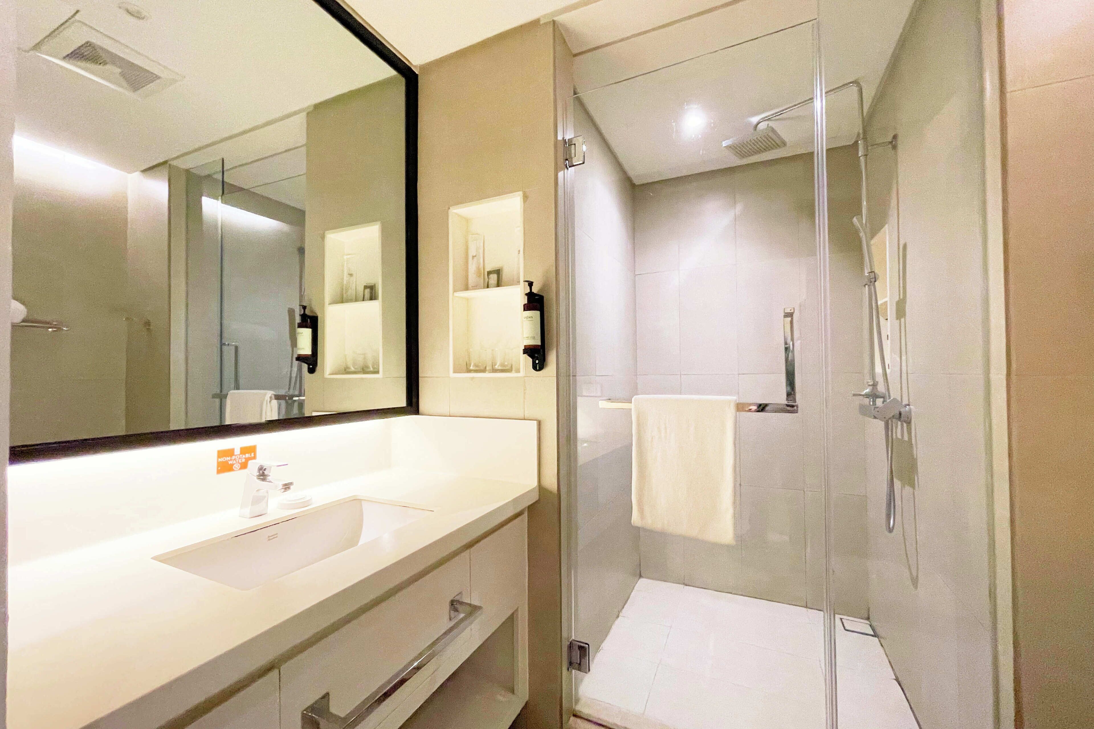A modern bathroom with a large mirror, a white sink, and a glass-enclosed shower area.