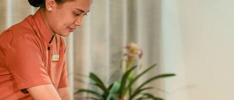 A massage therapy session in a spa setting with a client lying on a massage table, a therapist attending to the client, and a decorative vase with flowers in the background.