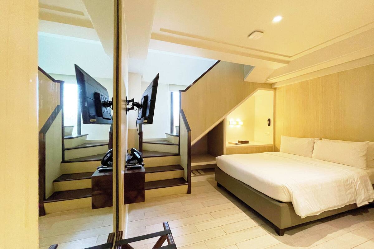 Habitación de hotel con cama, escritorio y teléfono, y una escalera que conduce a un piso superior.