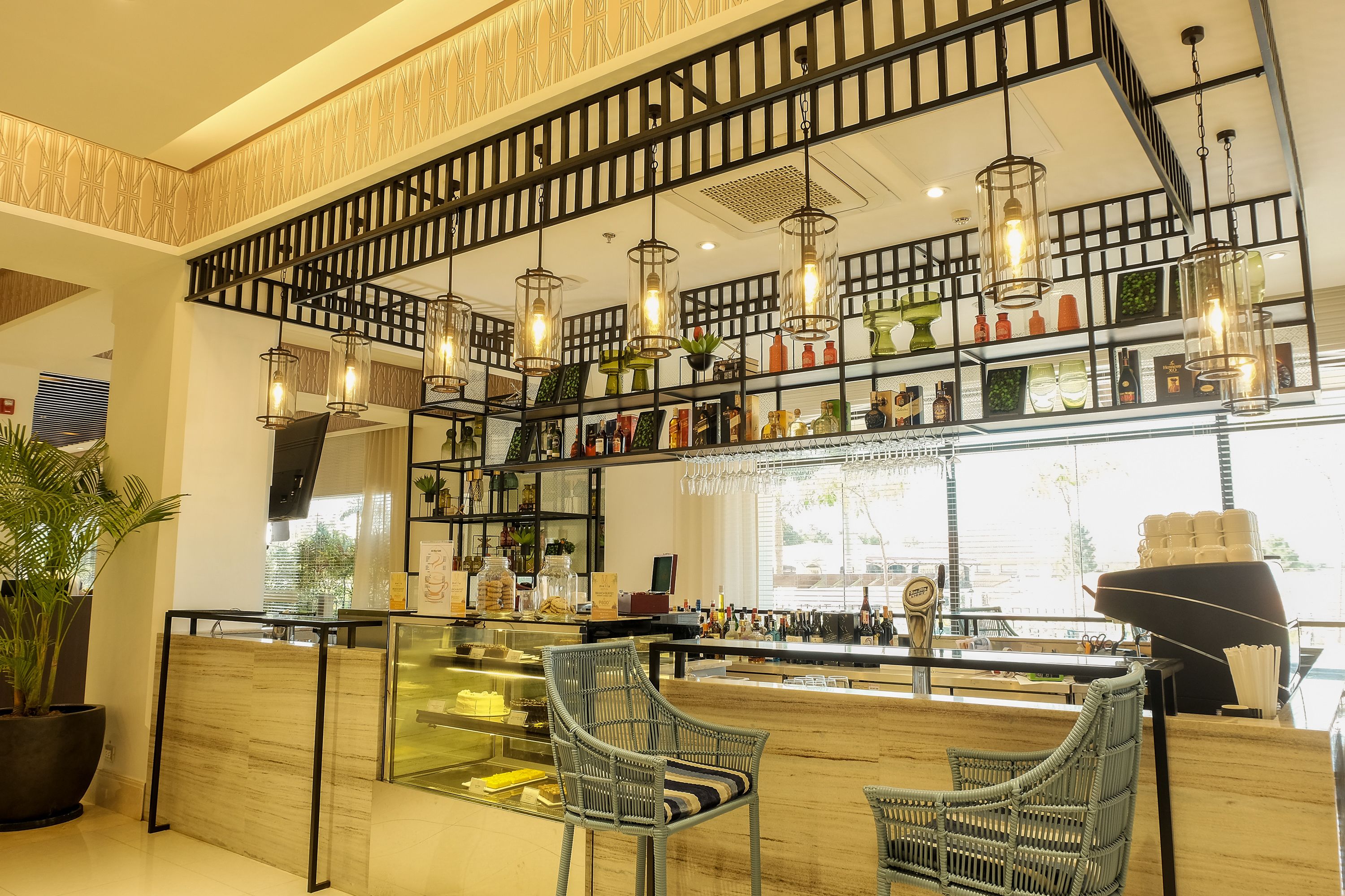 A modern bar area with wicker chairs, a glass counter, and various bottles and decorations.