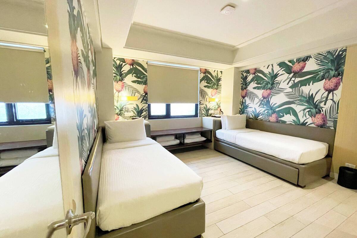 Habitación de hotel con dos camas, un espejo grande y papel tapiz tropical.