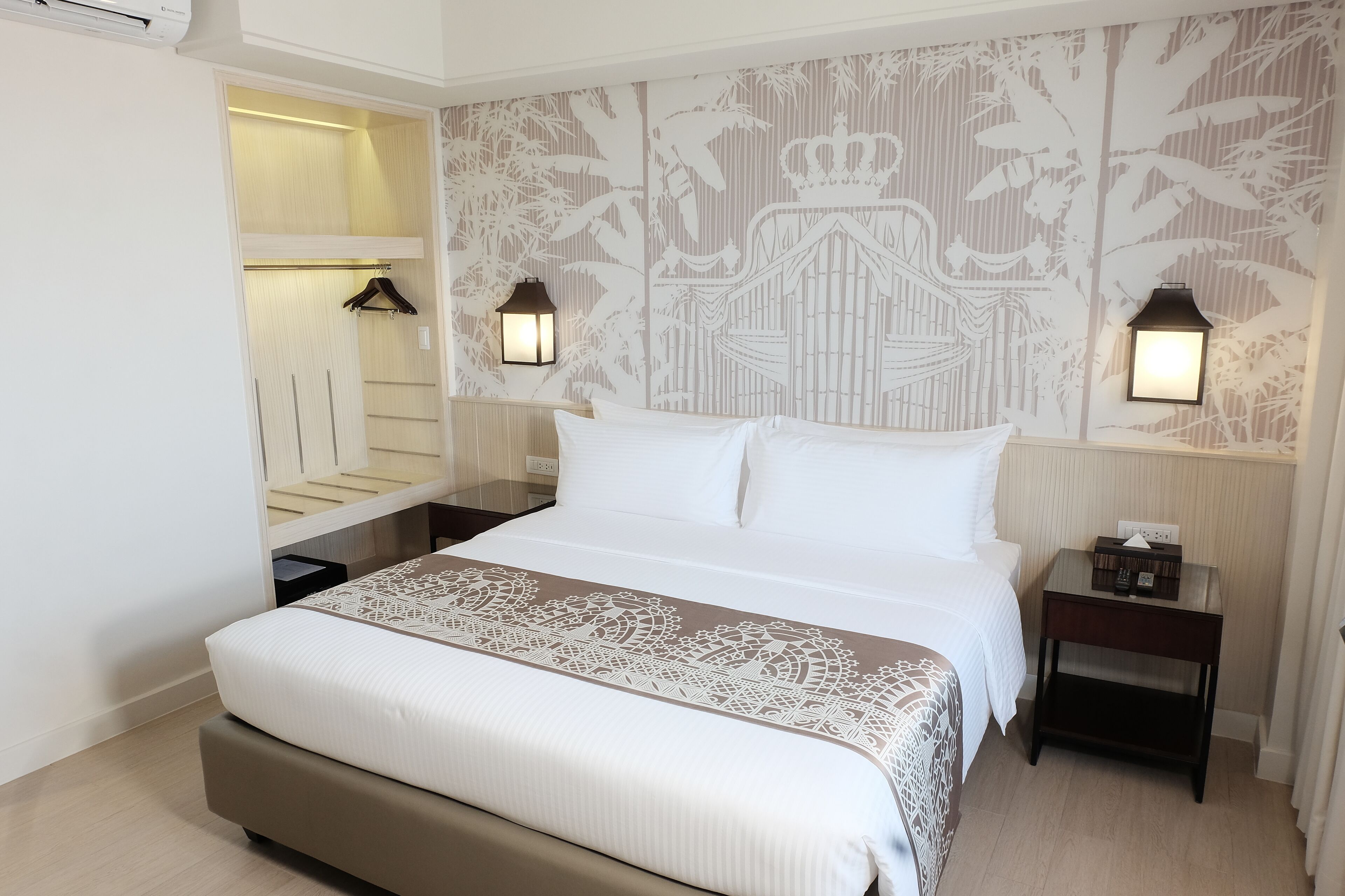 A neatly made bed with a patterned bedspread, a bedside table with a lamp, and a wall with a decorative panel.