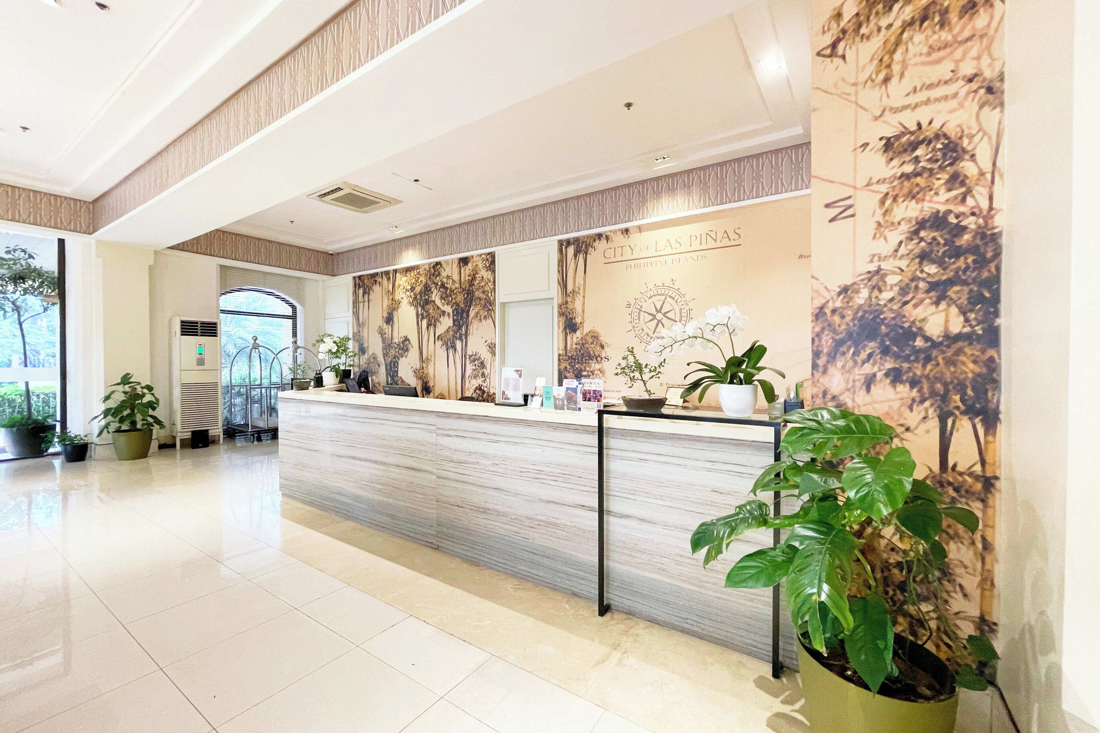 A hotel reception area with a marble counter, potted plants, and a large wall mural.