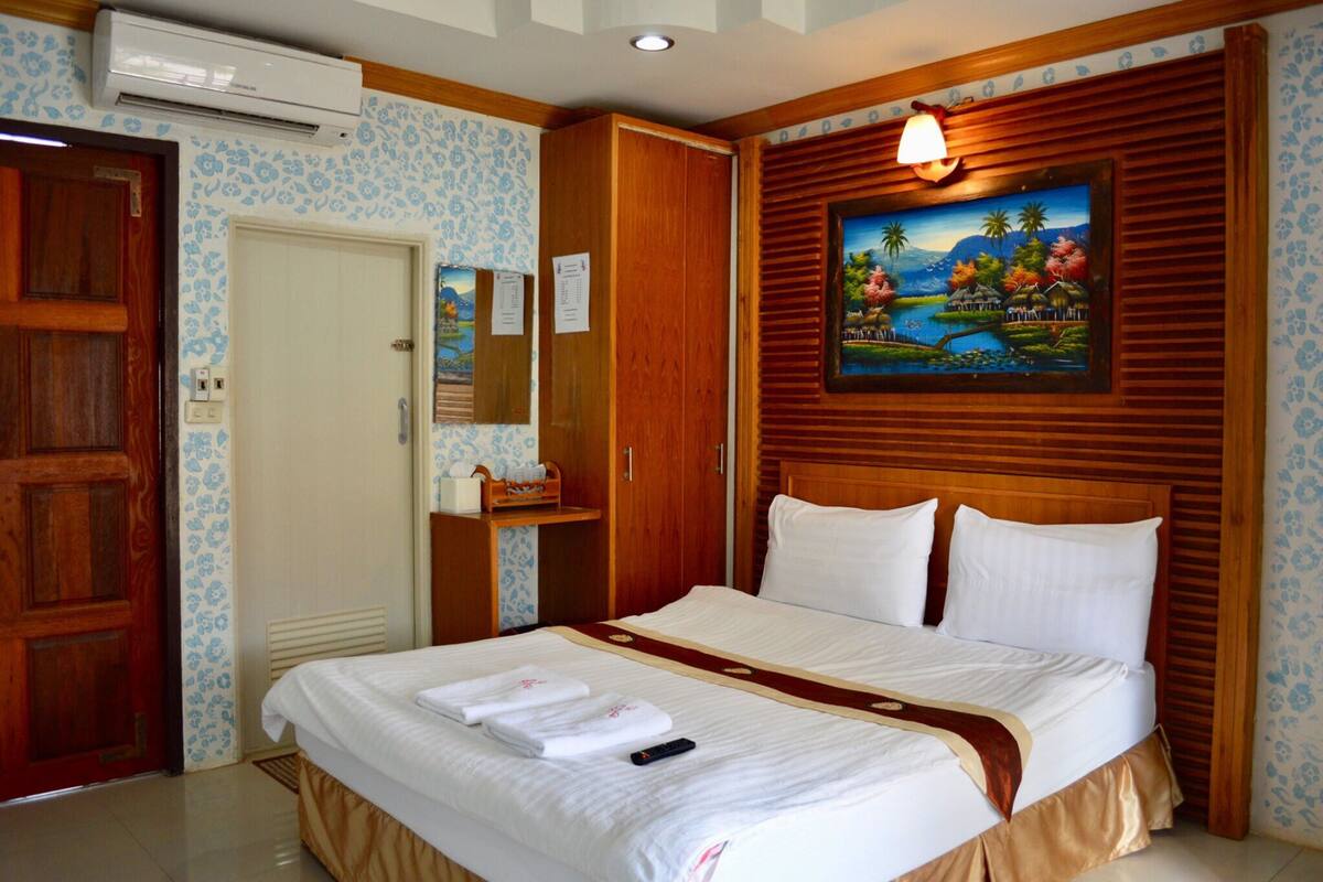 Une chambre d’hôtel avec un lit, une tête de lit en bois, un tableau, une armoire et une porte.