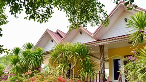 A house with a porch, surrounded by lush greenery and flowering plants. - Rachiga Hotel Grand Resort (Sawang Daen Din)