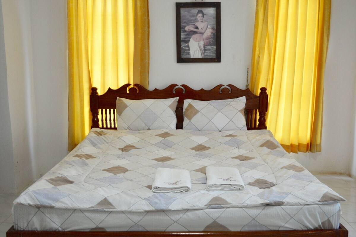 Un lit bien fait, recouvert d’une couvre-lit à motifs, avec deux serviettes pliées posées dessus.