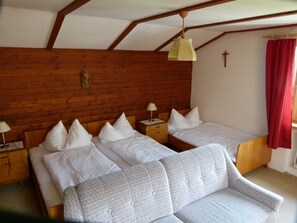 A room with two beds, a wooden ceiling, a cross on the wall, and a red curtain. - Triple Room (Type A) - Greber Christine - Frühstückspension Fernblick (Schoppernau)