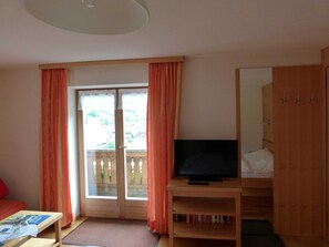 Ein Hotelzimmer mit Fernseher, einer Holzkabine mit Büchern, einem roten Sofa und einer Schiebeglastür nach draußen.