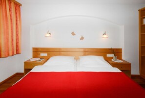 Ein Doppelbett mit roter Bettdecke, zwei Nachttische mit Lampen und ein hölzernes Kopfteil.