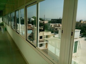 Un couloir doté de grandes fenêtres donnant sur un quartier résidentiel avec de nombreux immeubles et un ciel dégagé.
