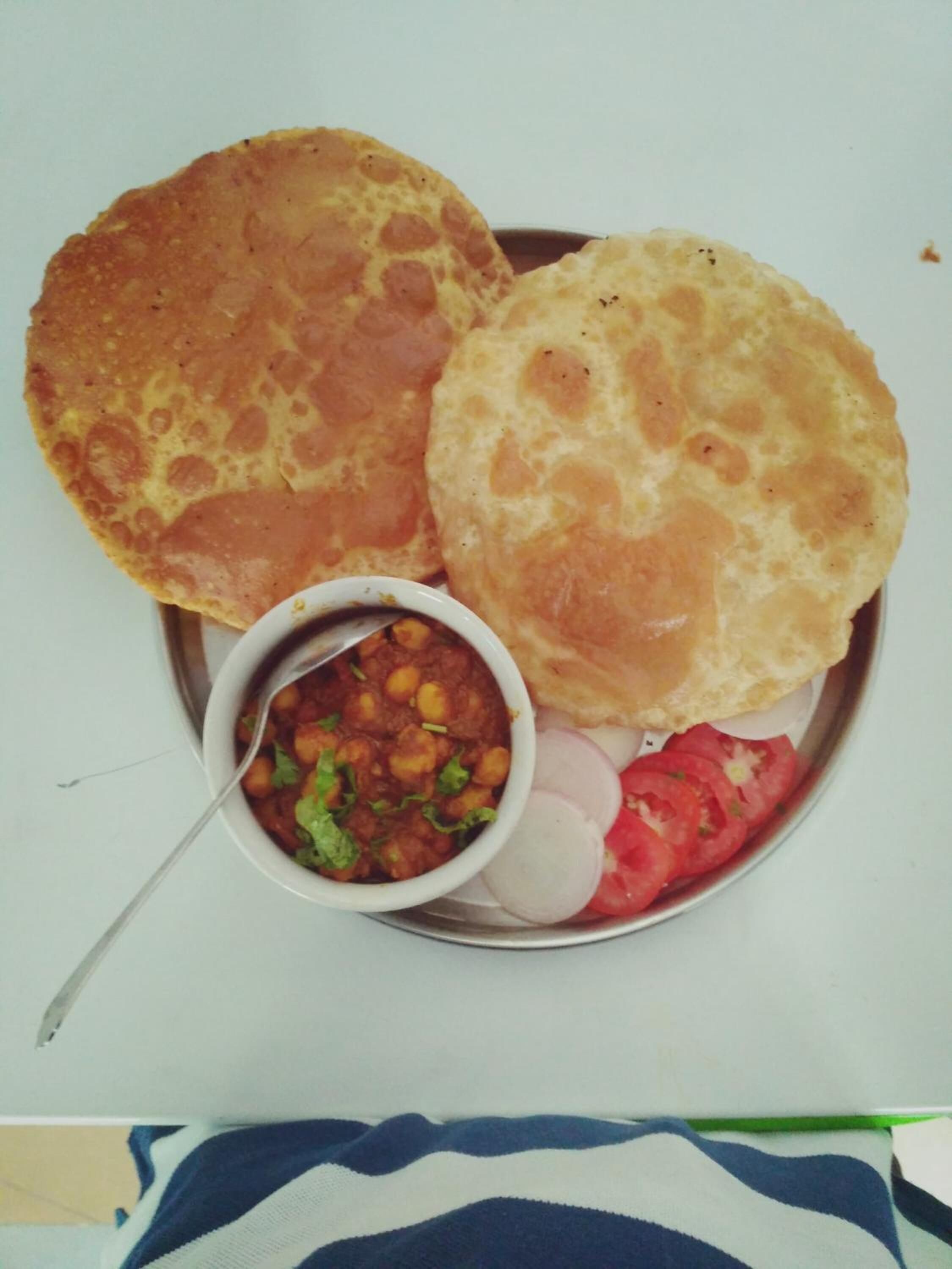 A plate with two types of bread, a bowl of chickpea curry, sliced tomatoes, and onions.
