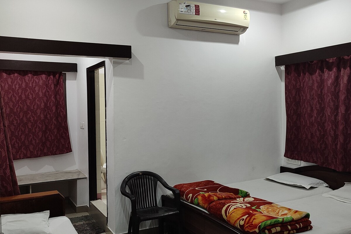 A bedroom with two beds, an air conditioning unit, a chair, and a desk.