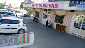 A building labeled "Hotel Ramnivas" with a signboard, a parked white car, and a scooter in front.
