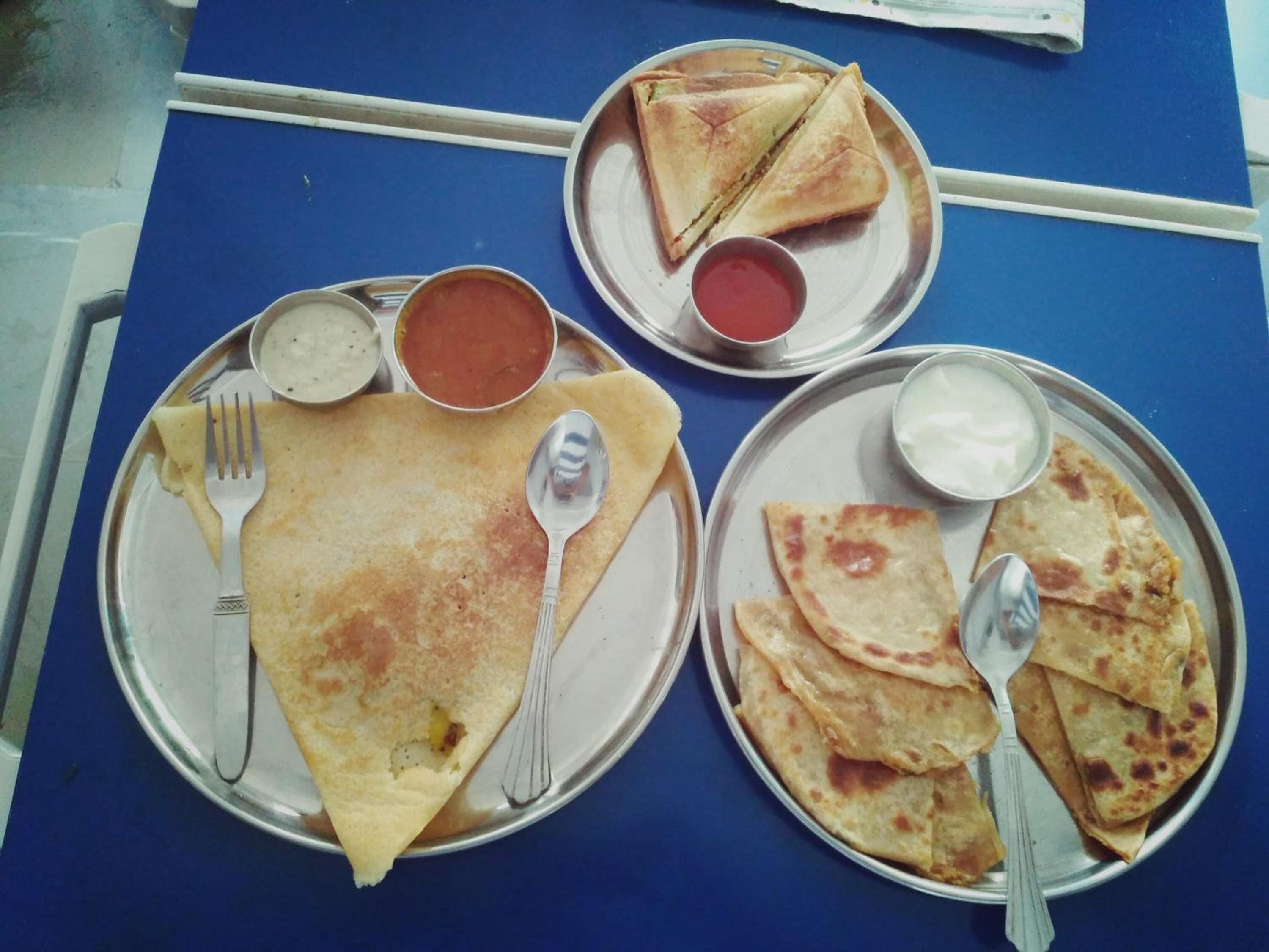 A meal consisting of crepes, a folded sandwich, and flatbreads served on metal plates with condiments.
