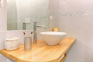 Ein Badezimmer mit einem Holzkosmetikschrank, einem weißen Waschbecken, einem Chromarmaturen und einem Spiegel mit Fliesenrückwand.