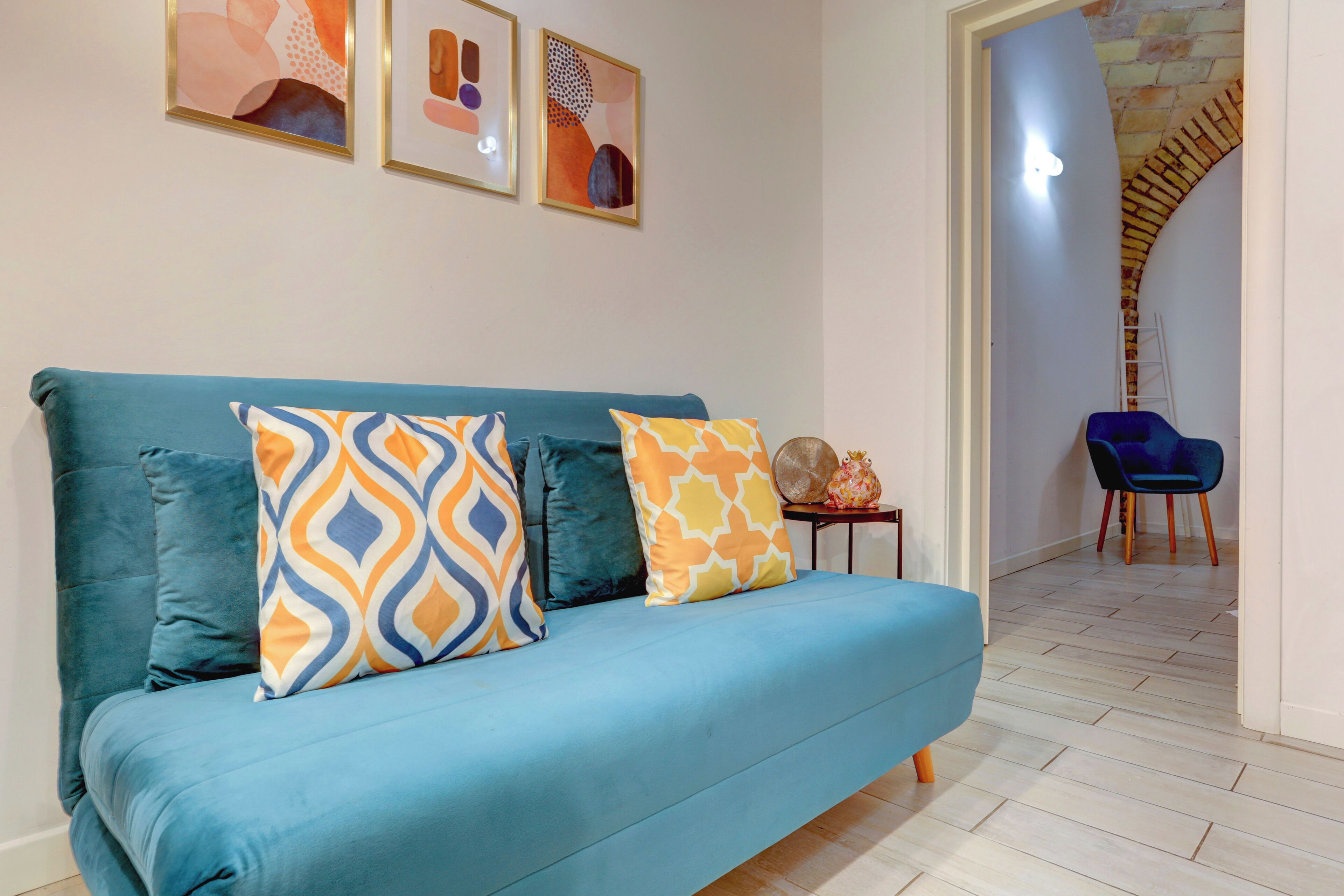 A modern living room with a teal sofa, patterned cushions, and abstract wall art.