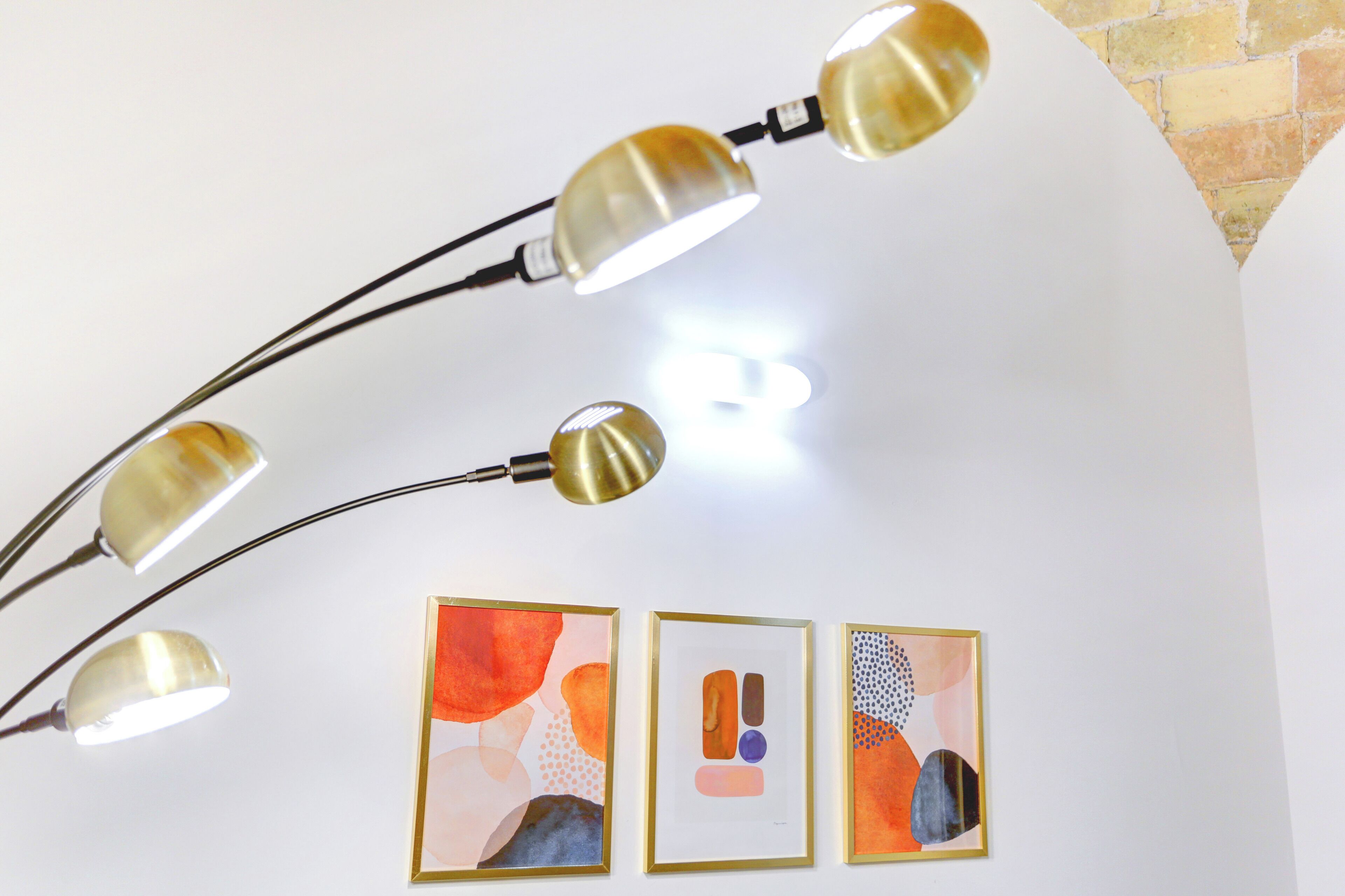 A ceiling with three pendant lights and three framed abstract paintings.