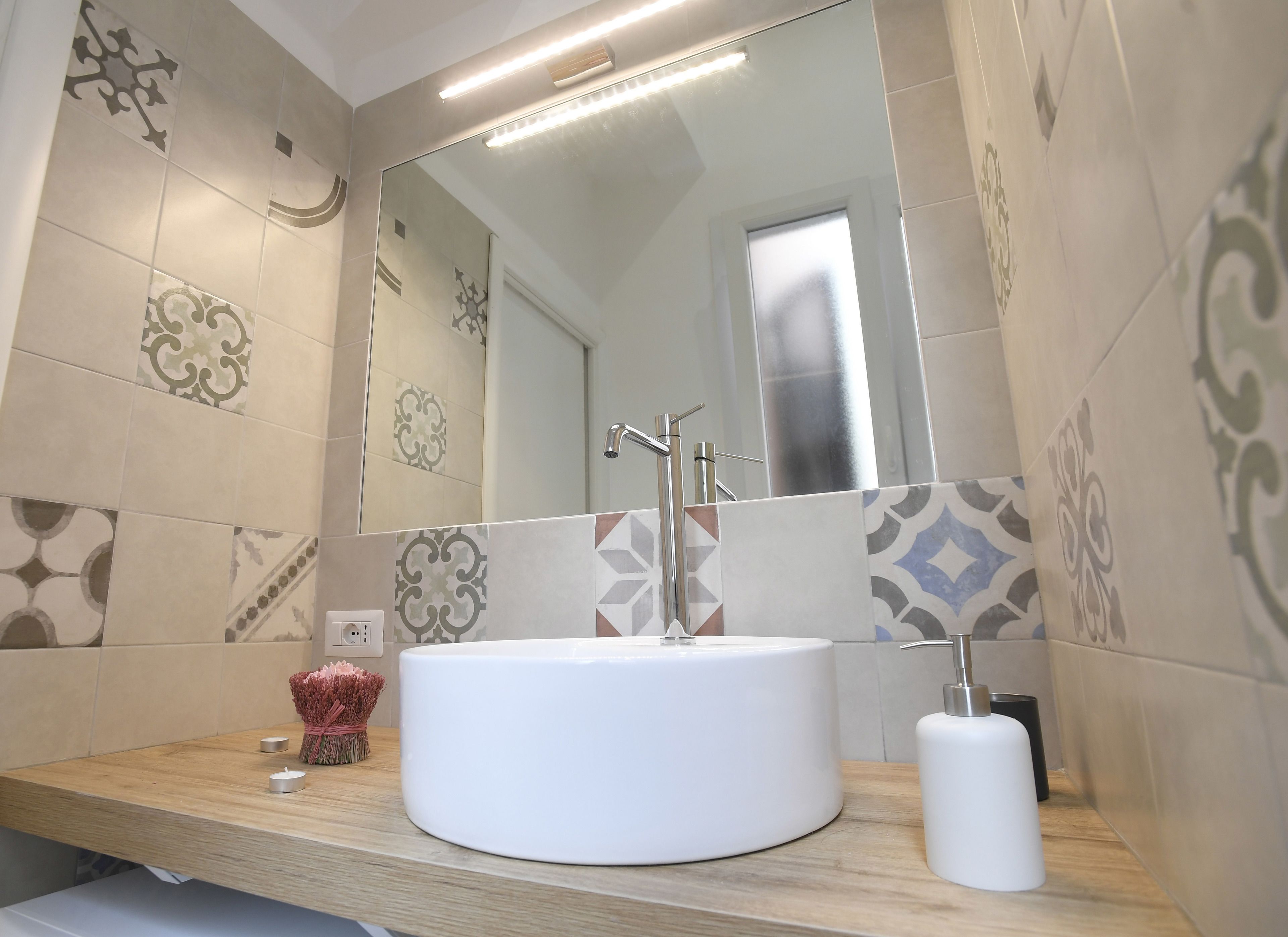 Une salle de bain moderne avec un lavabo rond blanc, un miroir et des carreaux à motifs.