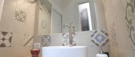 Une salle de bain moderne avec un lavabo rond blanc, un miroir et des carreaux à motifs.
