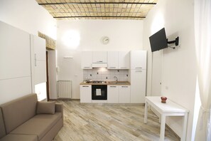 Eine kleine Küche mit weißen Schränken, einem Einbauofen und einem flachbildfernseher an der Wand.