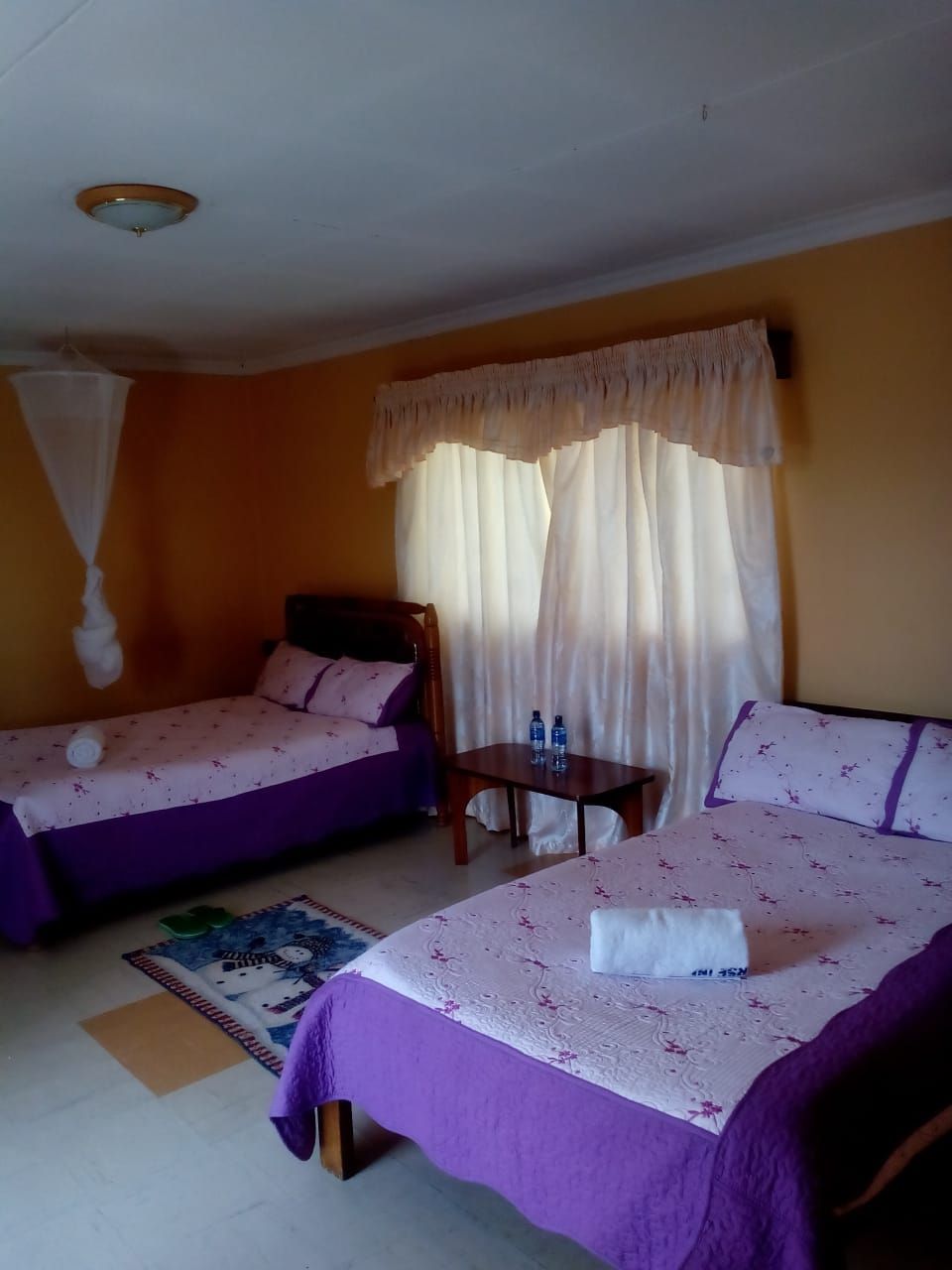 A hotel room with two beds, a small table, and a window with curtains.