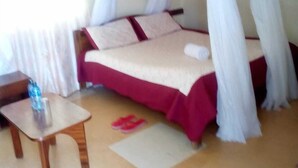 A bedroom with a bed, a nightstand, and a window with curtains. - Racecourse Inn Hotel (Eldoret)