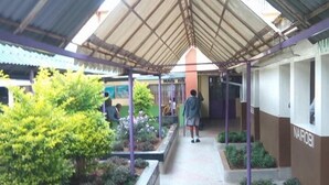 A covered walkway with a metal roof, surrounded by greenery and a building labeled "NAIROBI". - Racecourse Inn Hotel (Eldoret)