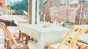 A dining area with a table covered by a green tablecloth, wooden chairs, and a view of a rustic building through a window. - one step to heaven inn (Zhangjiajie)