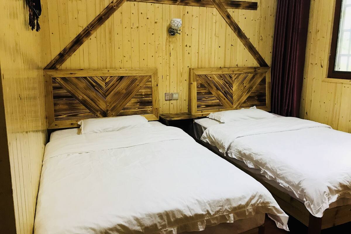 A room with two beds, wooden walls, and a window with curtains.