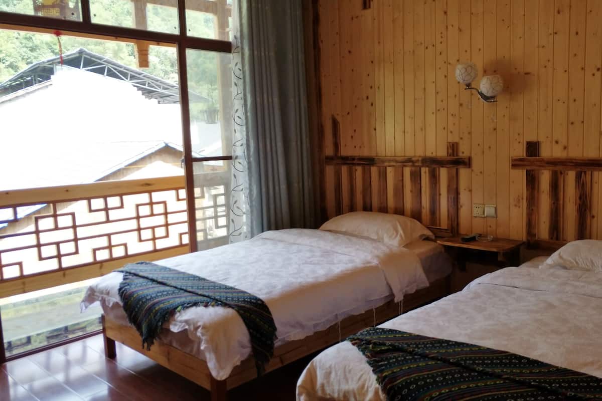 A room with two beds, wooden walls, a window with a view of a building, and a curtain.