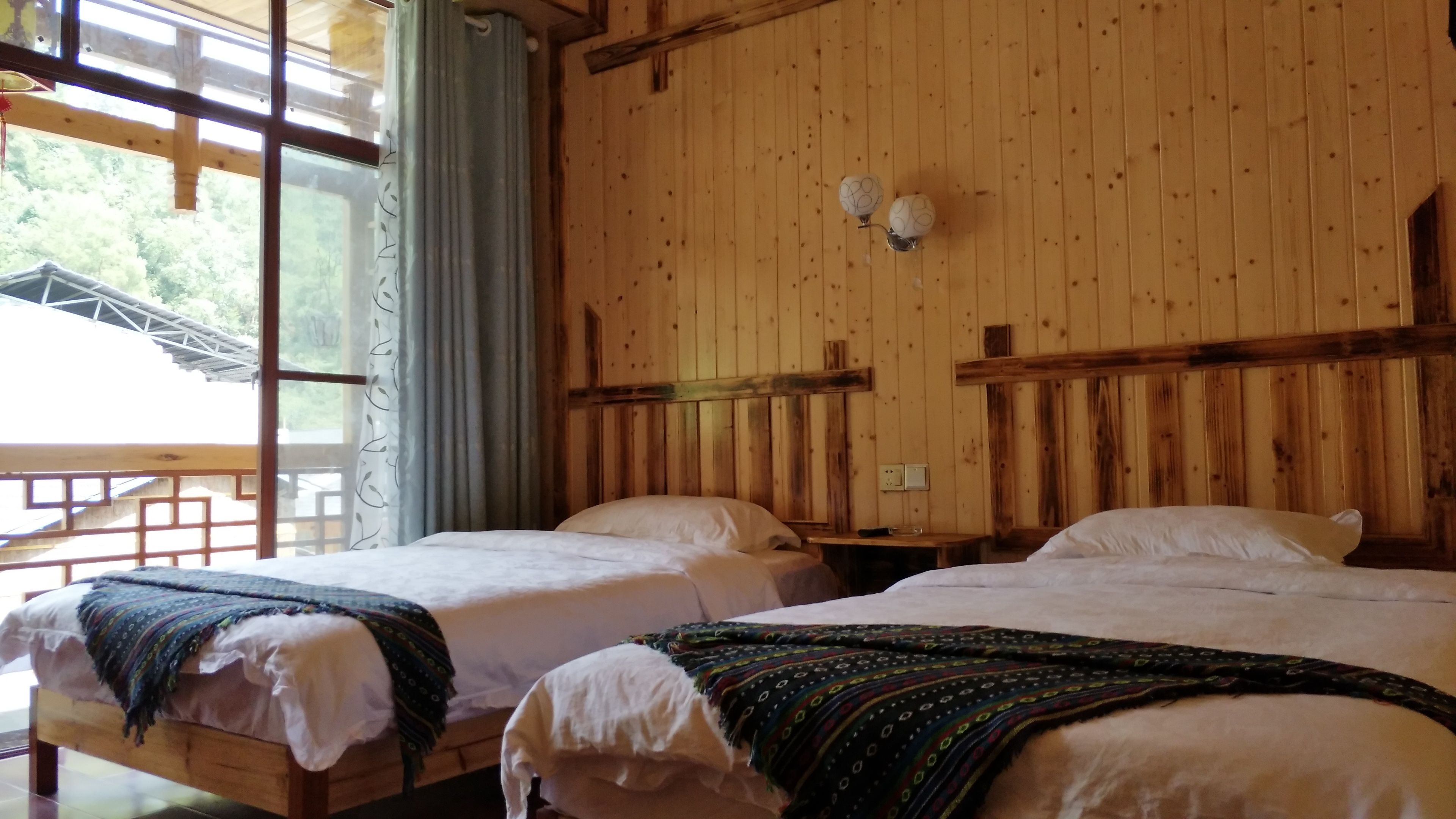 A wooden room with two beds, a window with curtains, and a wooden ceiling.