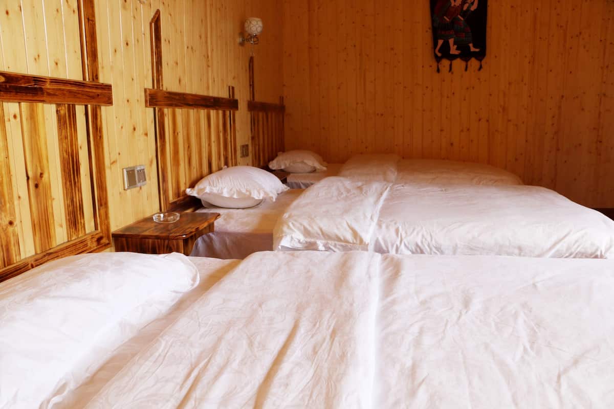 A wooden room with three beds, a nightstand, and a wall-mounted light fixture.