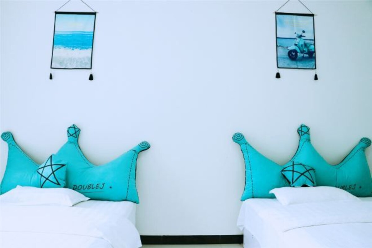 A room with two beds, each with turquoise pillows and a star design, and a wall with two framed pictures.