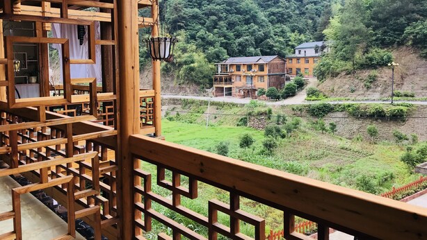 A wooden balcony with a view of a hillside with houses. - one step to heaven inn (Zhangjiajie)