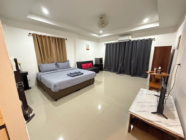 Una habitación de hotel moderna con una cama grande, un escritorio con computadora, un televisor y un ventilador de techo.