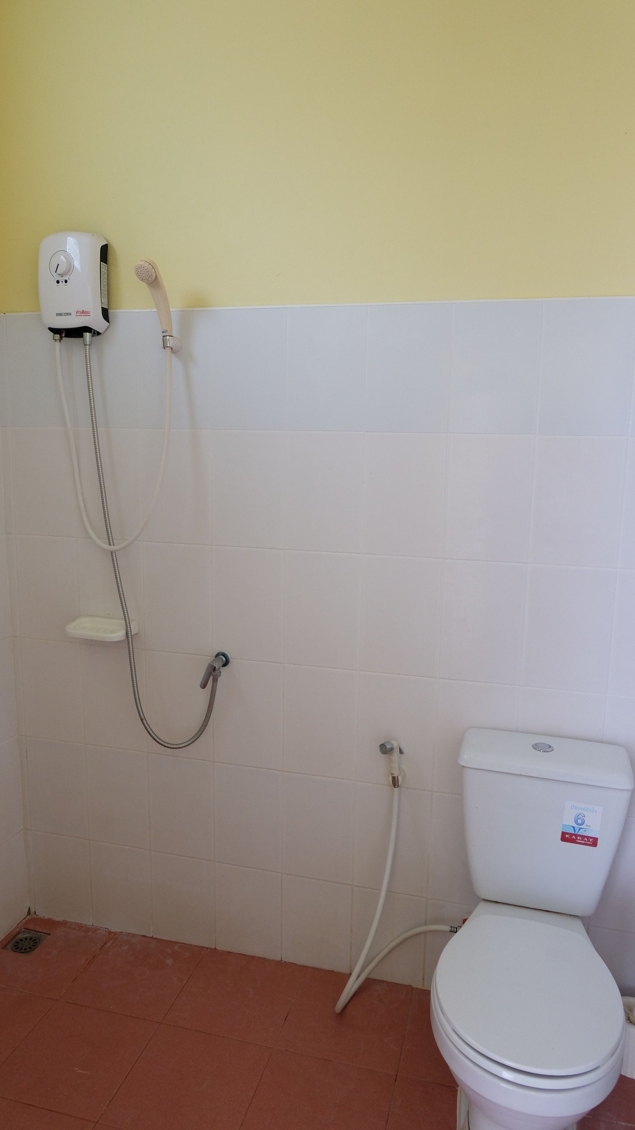 A bathroom with a toilet, a shower unit, and a white tiled wall.