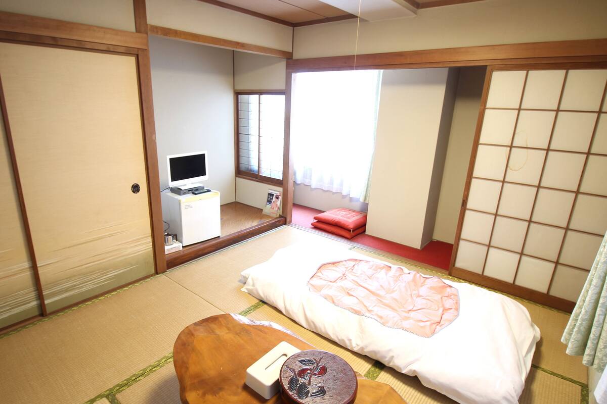 A traditional Japanese-style room with tatami flooring, a futon bed, a small wooden table, and sliding doors.
