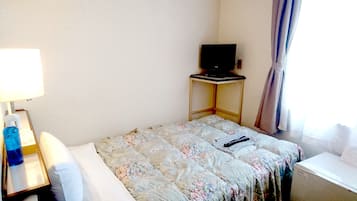 A hotel room with a bed, a desk with a lamp, a television on a small table, and a window with curtains.