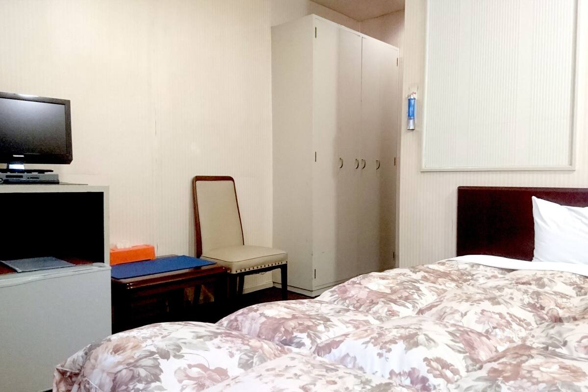A hotel room with a bed, a desk with a computer, a chair, a wardrobe, and a television.