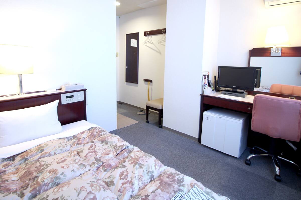A hotel room with a bed, a desk with a computer, a chair, and a TV.