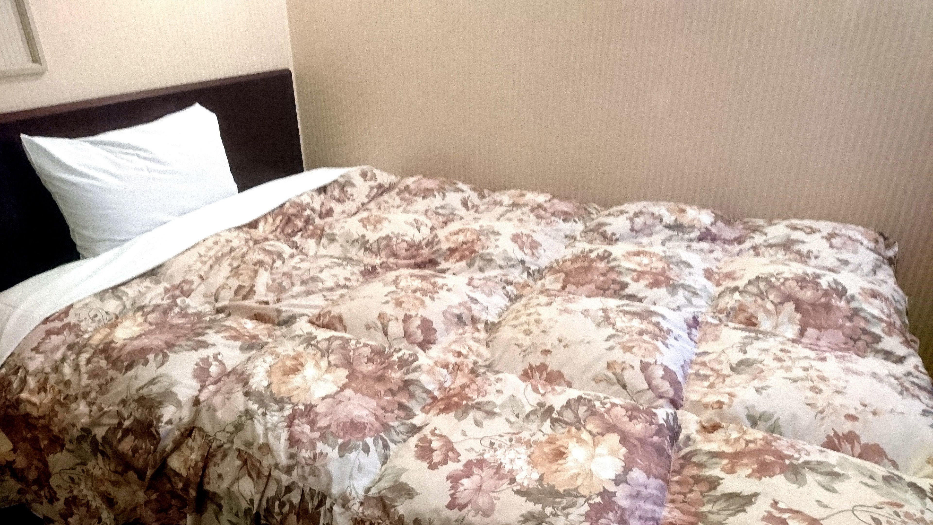 A bed with a floral comforter and a white pillow.