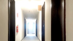 A narrow hallway with doors on both sides, a fire extinguisher on the left, and a bright exit at the end. - Royal Inn Shinyamaguchi (Yamaguchi)