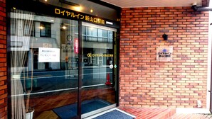 A building entrance with a glass door, a brick wall, and a sign in Japanese. - Royal Inn Shinyamaguchi (Yamaguchi)