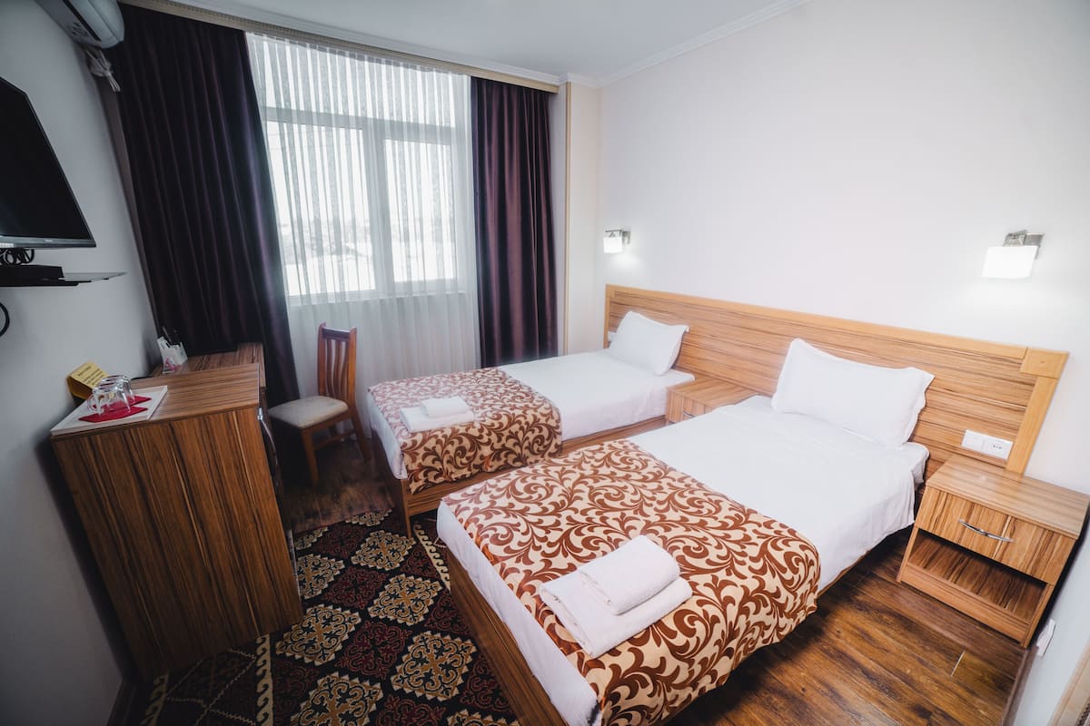 A hotel room with two beds, a desk, a chair, a TV, and a window with curtains.