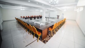 Un amplio salón de conferencias con una larga mesa y sillas naranjas, paredes blancas y un candelabro.