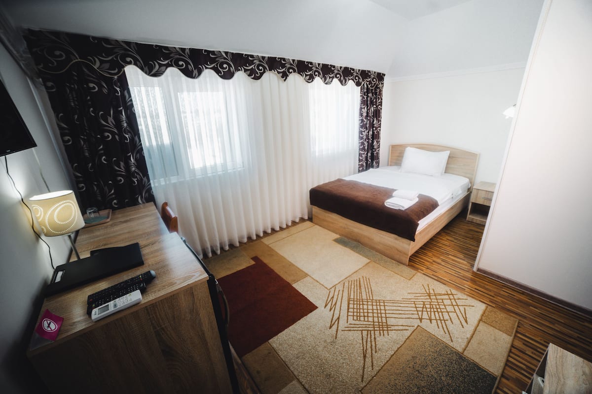 A hotel room with a bed, a desk with a lamp, and a window with curtains.