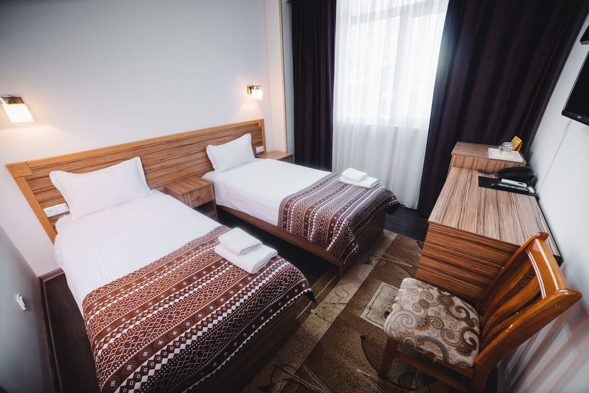 A hotel room with two beds, a desk, a chair, and a TV.